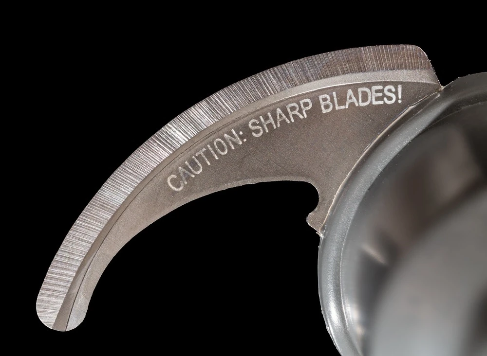 Close-up of a metallic, circular blade with “CAUTION: SHARP BLADES!” engraved on it.