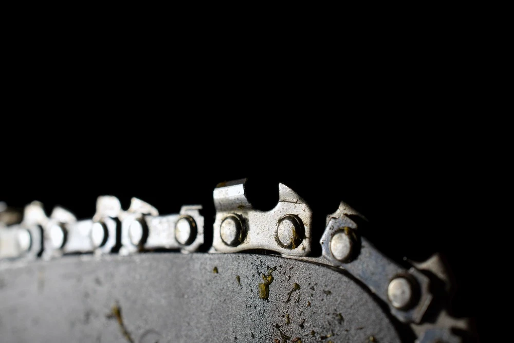 Close-up of a dirty, metallic chainsaw blade against a dark background